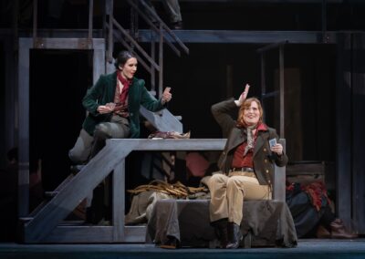 Two women in period costumes playing cards on a stage set. From the opera "Carmen" at the Edmonton Opera 2023.