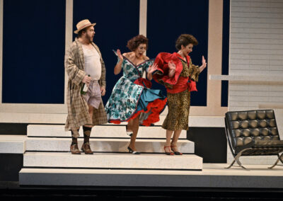 Two opera singers in elaborate gowns perform with emotion, on a stage. One older male opera singer in a house robe to the left of them. From the opera "La cenerentola" with the Manitoba Opera 2022.
