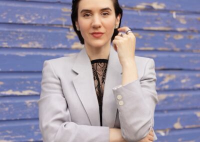 Woman in blazer and jeans poses against blue wall