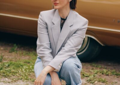 Woman in blazer and jeans crouching by vintage gold car.